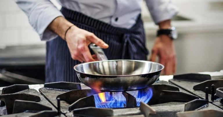 A chef is cooking on a stove with blue flames.