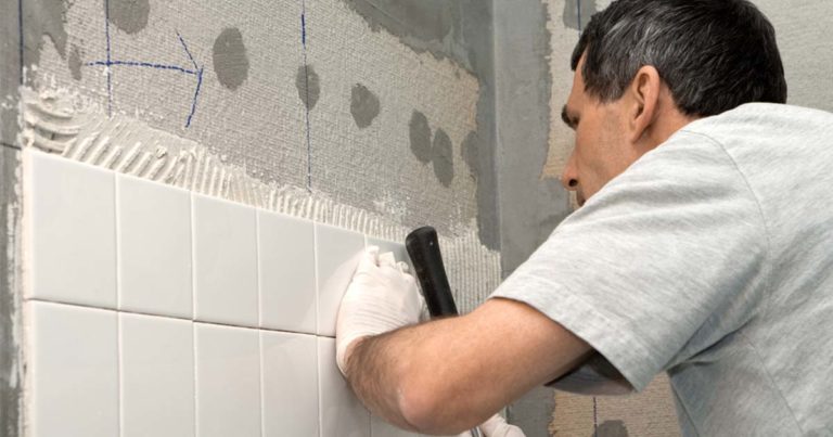 man installing bathroom tiles on wall