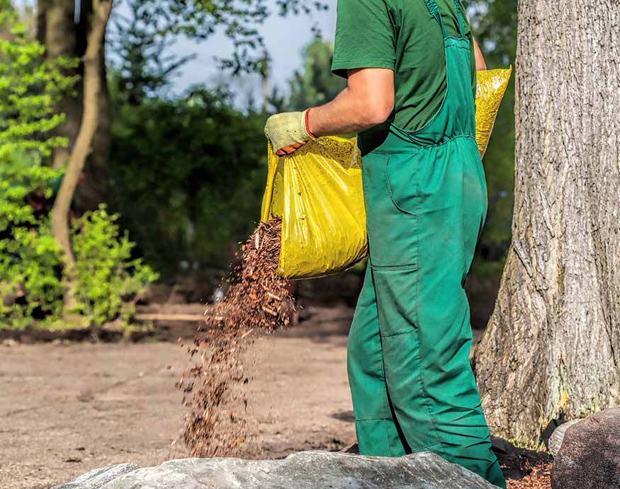 A gardener adding a bag of bark mulch 