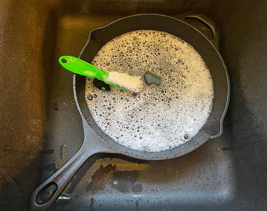 a coarse bristled brush on a cast-iron skillet filled with soap and water mix