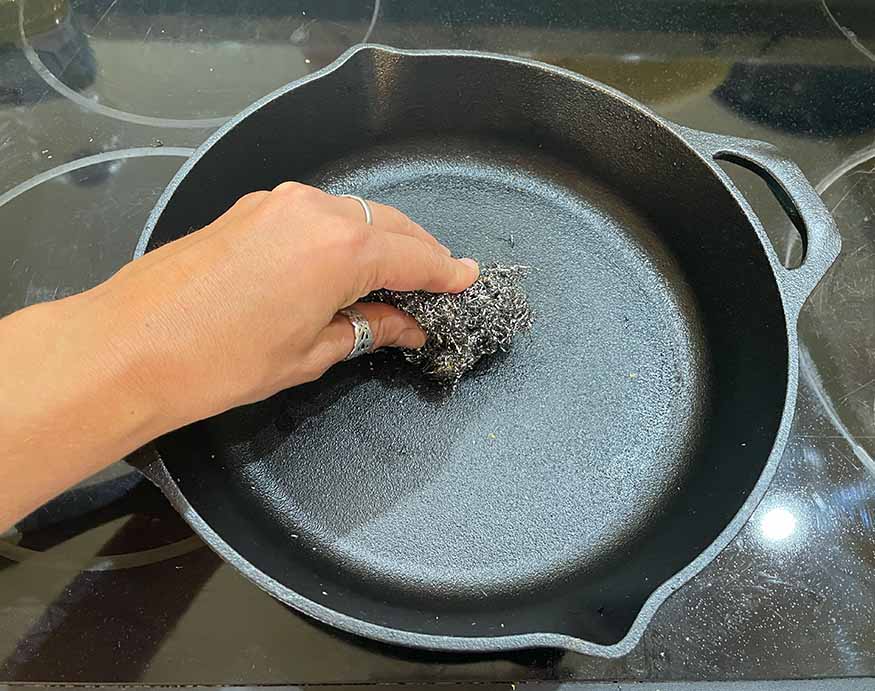 using a steel wool to remove rust on a cast iron skillet