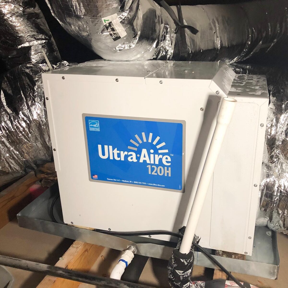 Ultra-Aire 120H dehumidifier installed in an attic, surrounded by insulated ductwork and a metal tray.