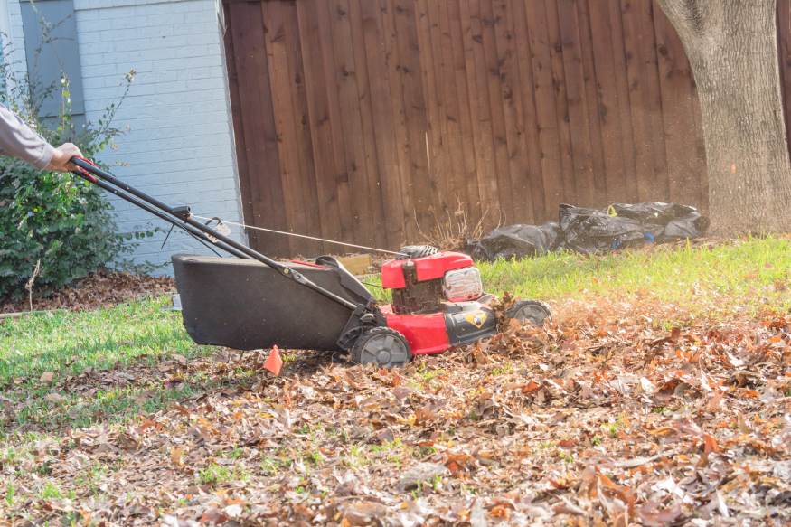a person pushing a lawnmower to mulch the leaves