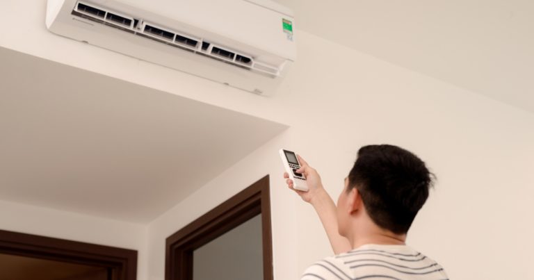 a person using a remote to turn on the wall-mounted AC