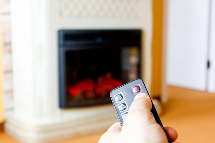 A person using the remote the increase the heat output of a wall mounted electric fireplace
