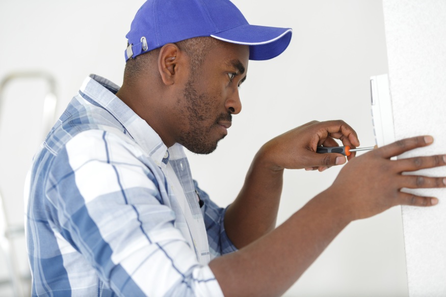 A man in a blue hat is working on a light switch.