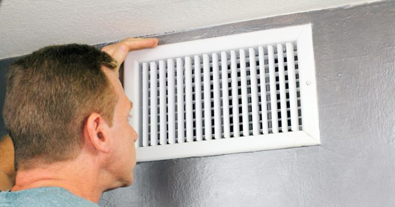 A man inspecting a vent in a bathroom.
