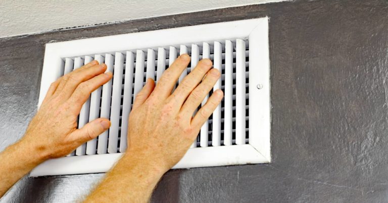 A person putting his two hands in front of an air vent to check the cold air