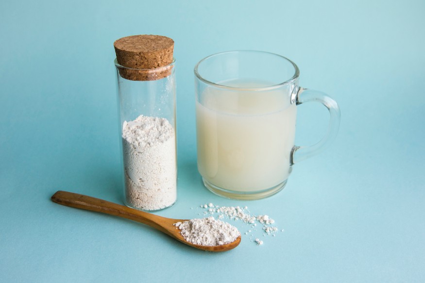 a container diatomaceous earth powder next to a spoon and glass of water