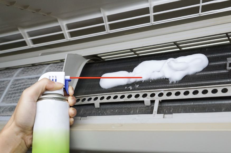a person spraying a foam cleaner to the AC’s dirty coils