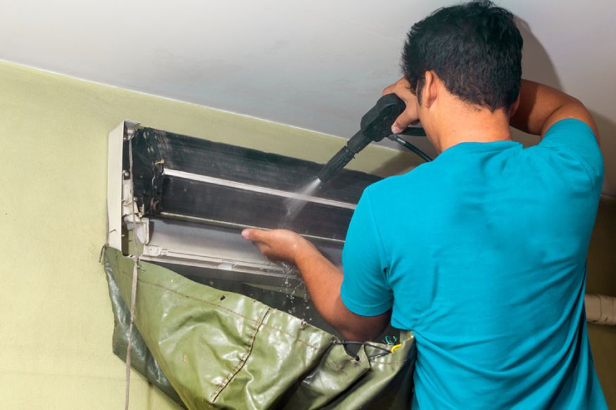 a technician using a water pressure to rinse the AC coils