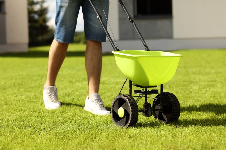 a man using a lawn spreader to scatter pre-emergent weed killer