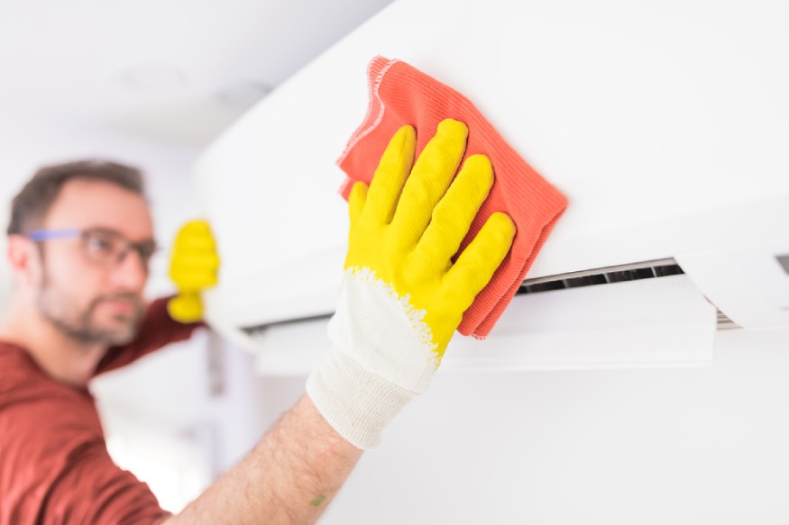 A man cleaning an air conditioner with yellow gloves.
