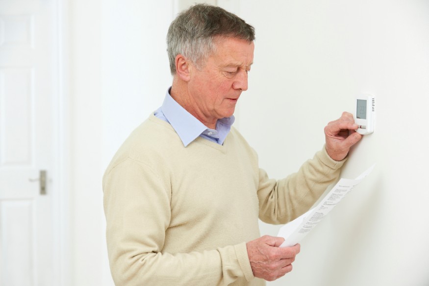 man adjusting the thermostat while looking at his electricity bill