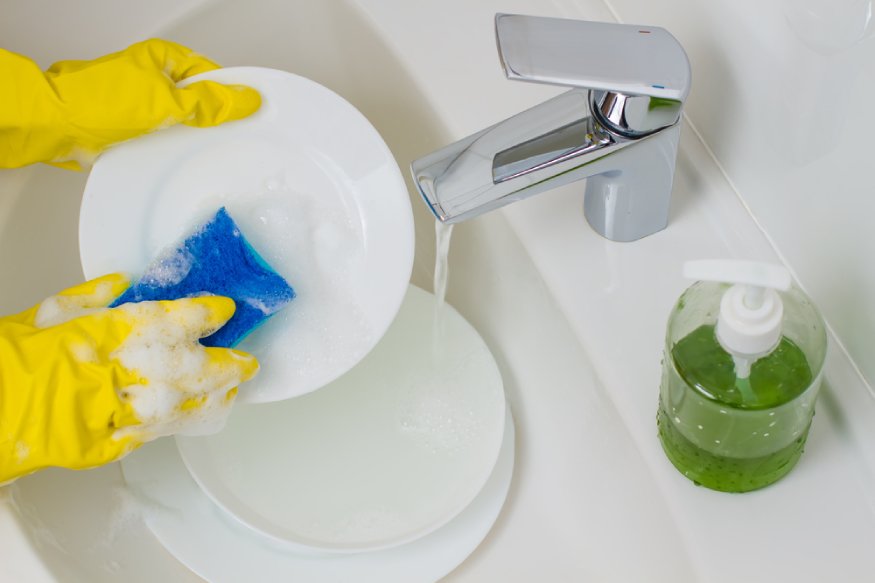 A person in yellow gloves washing a plate in a sink.