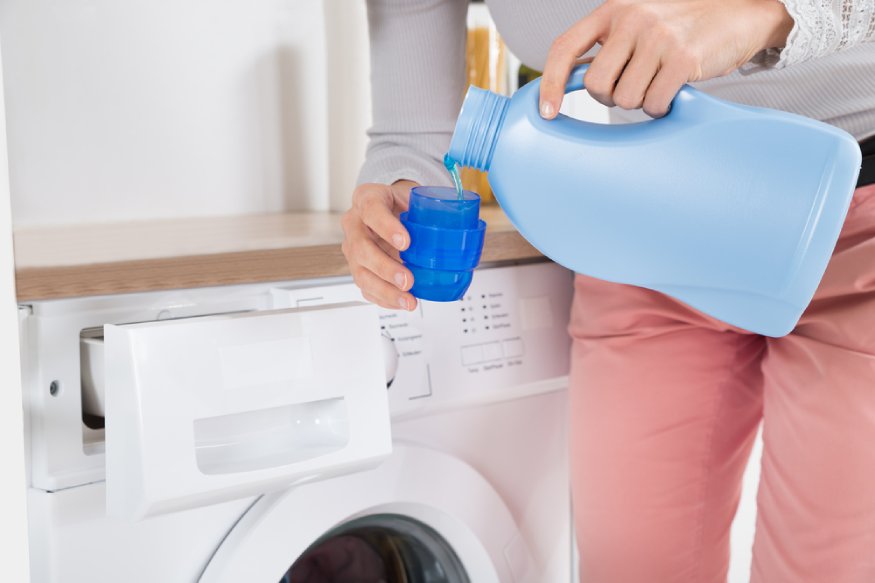 A woman filling a blue jug into a washing machine.