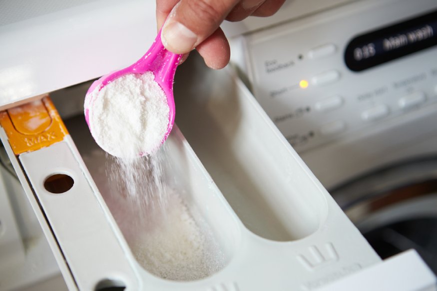 A person is pouring powder into a washing machine.