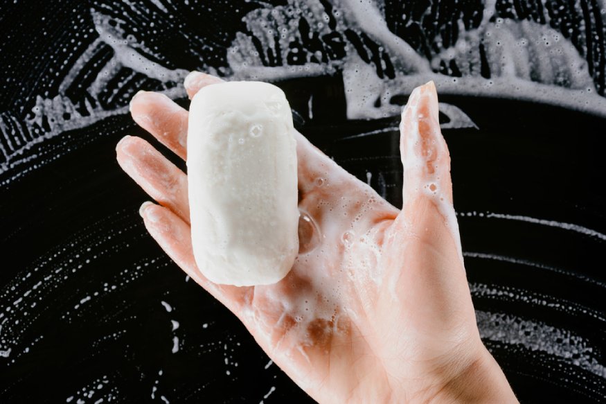 A woman's hand is holding a soap bar in front of a black background.