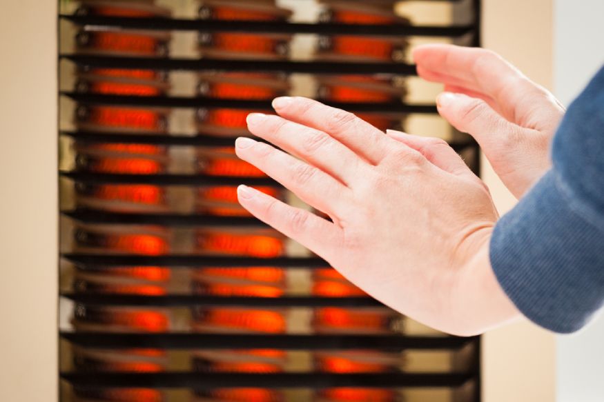 a woman warming her hands next to a space heater