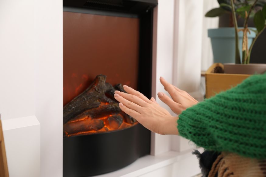 woman putting her hands in front of the electric fireplace
