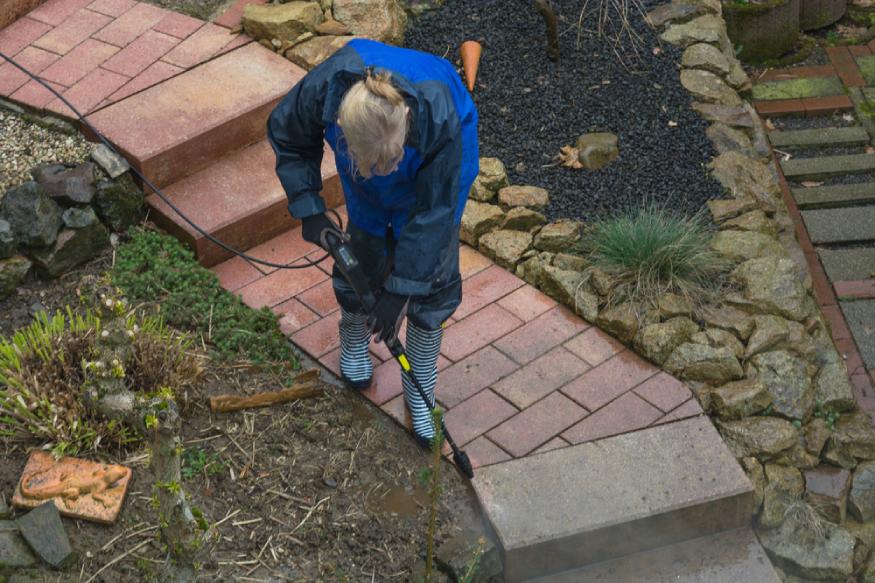 man using a pressure washer to clean the pathway