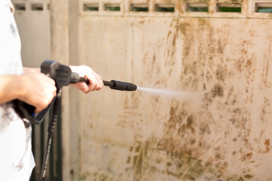 woman using a pressure washer to clean the wall
