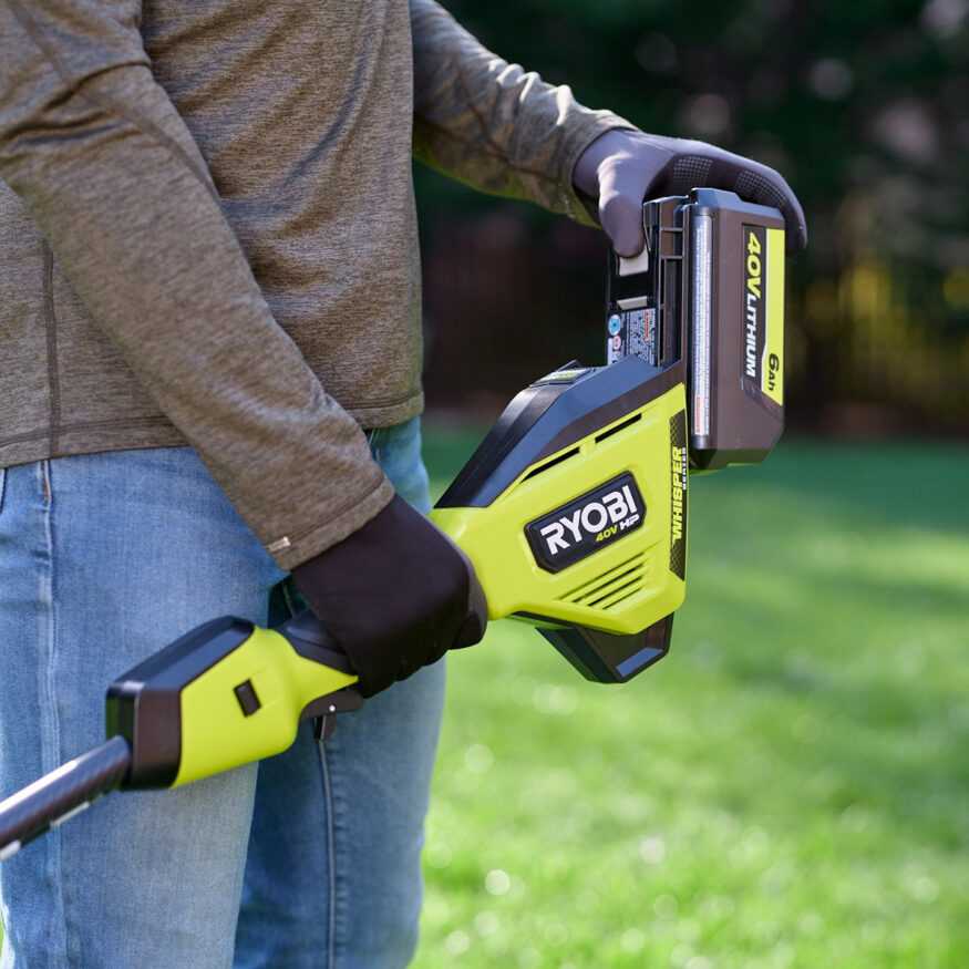 man plugging a ryobi battery pack into a string trimmer