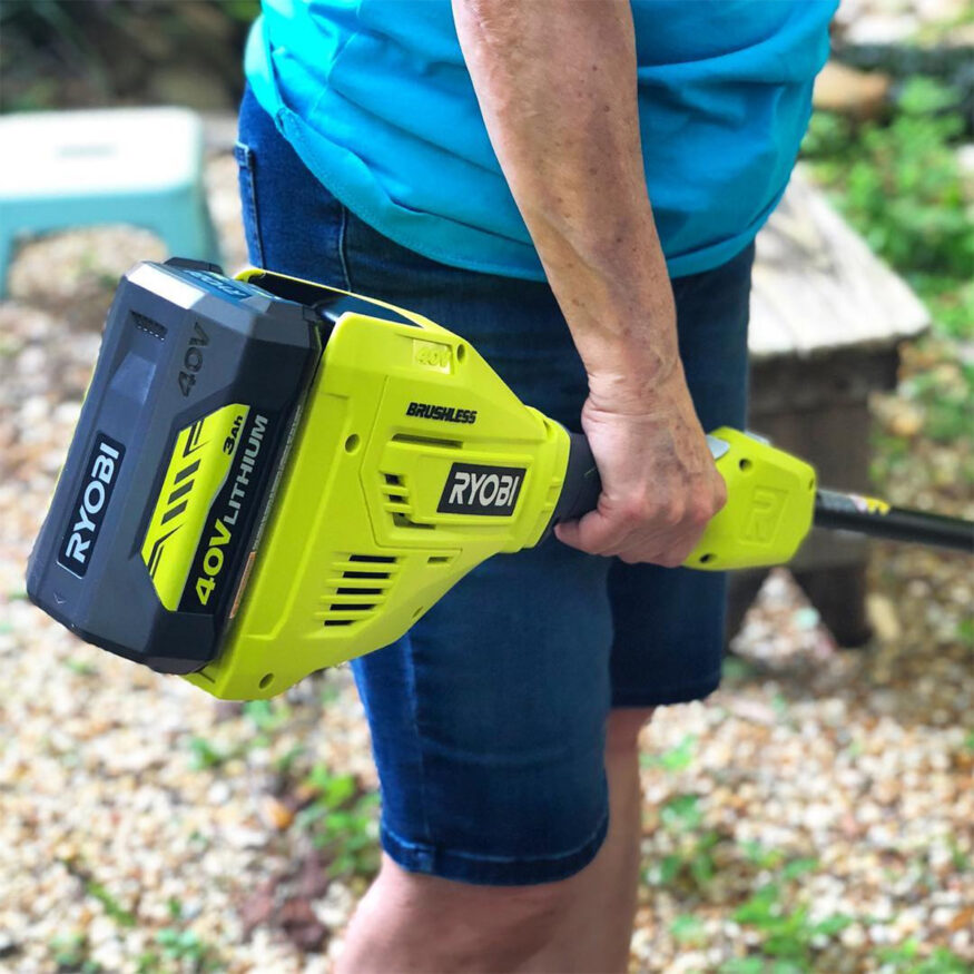 A woman holding a ryobi electric hedge trimmer.