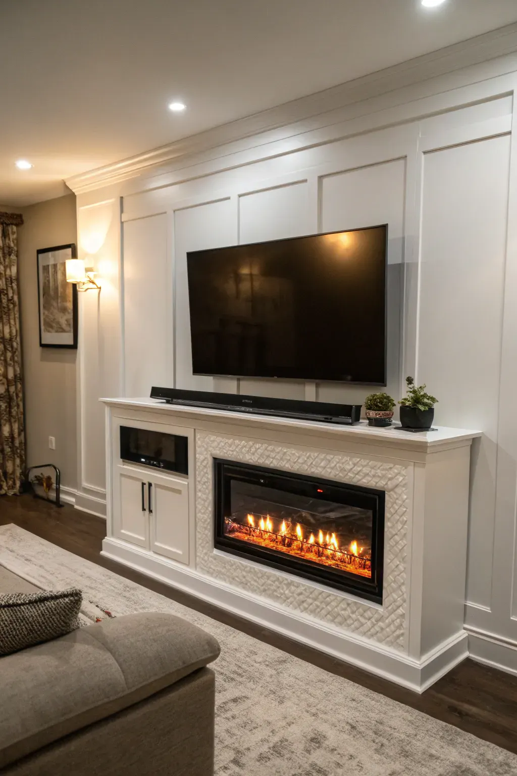 A modern living room with a wall-mounted TV above a white electric fireplace, a soundbar, small plants, and a patterned area rug.