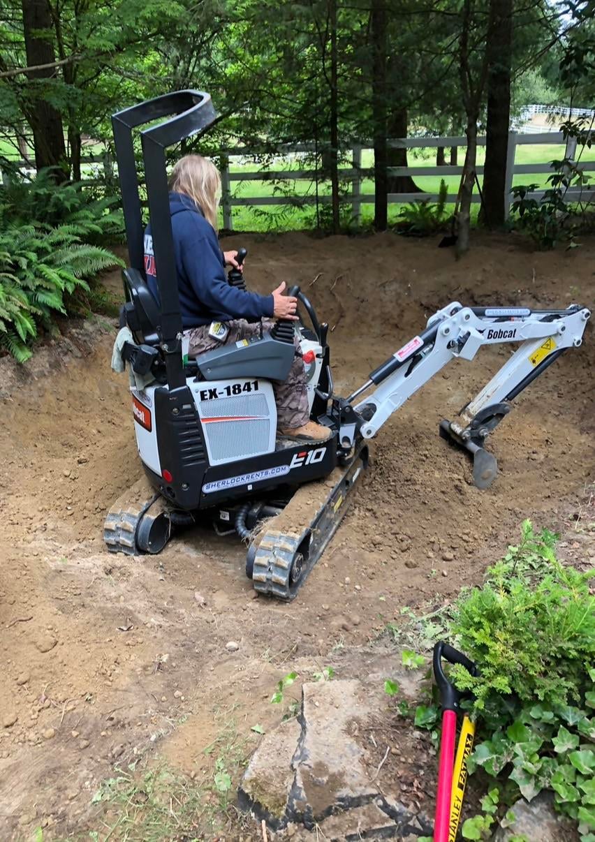 Builder digging the sunken fire pit with a rented mini excavator