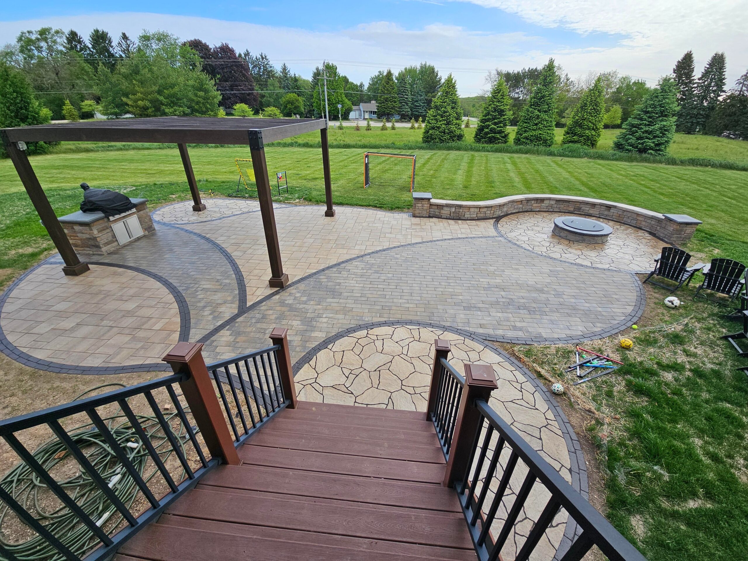 Aerial view of a paver patio with round fire pit, curved seat wall, pergola and grill island