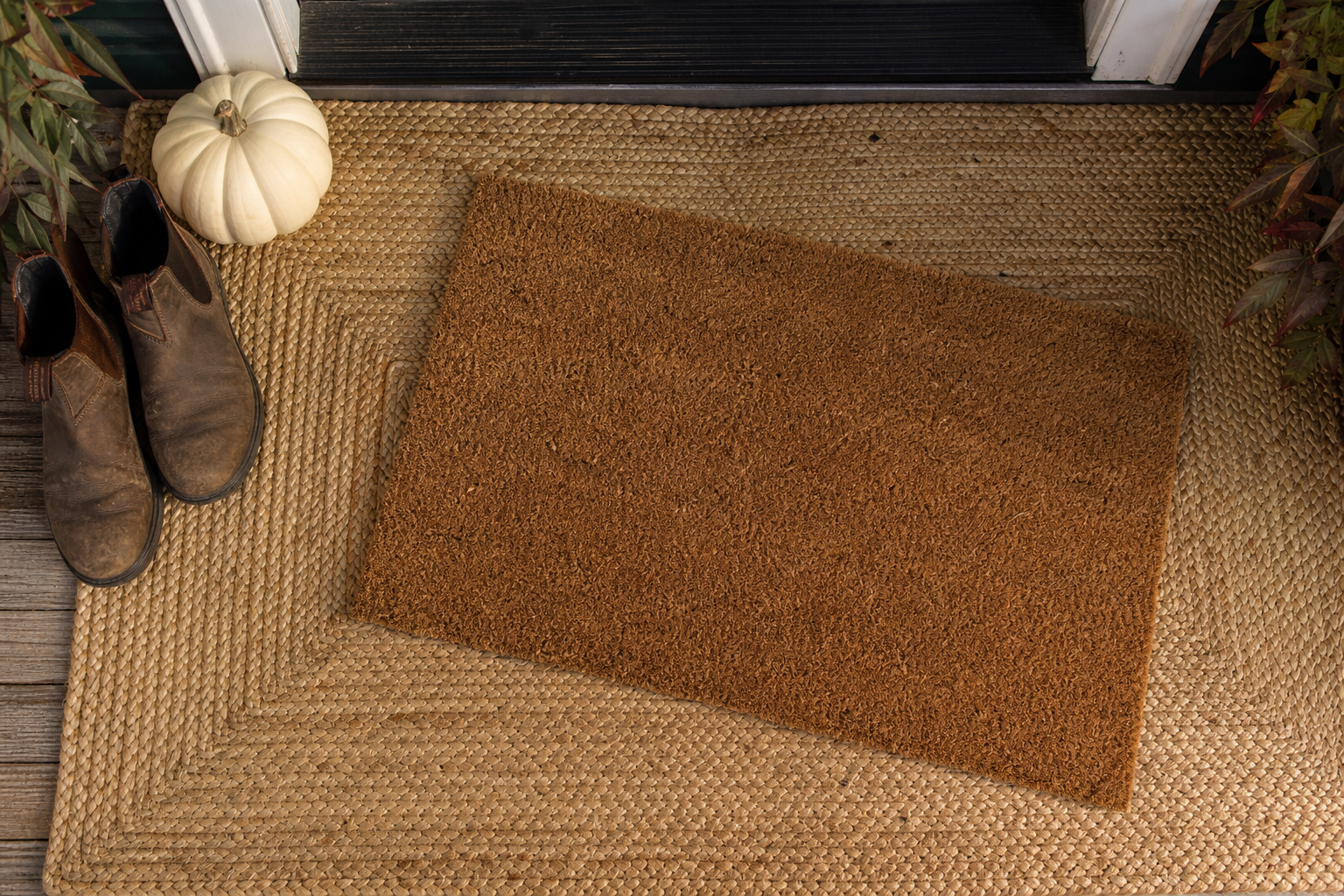 A woven jute outdoor rug at a front door with a smaller coir doormat layered on top at an angle