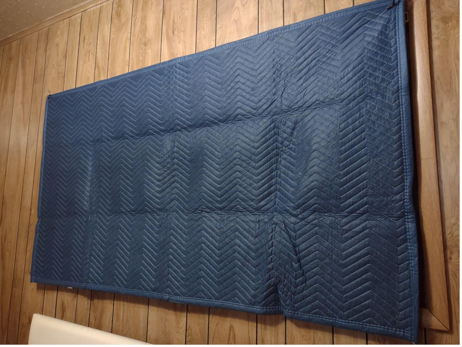 Blue quilted moving blanket hung over a window on a wood-panelled wall