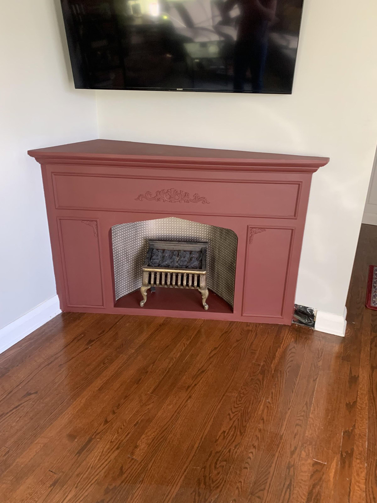 Dusky pink corner faux fireplace with a vintage insert under a wall-mounted TV